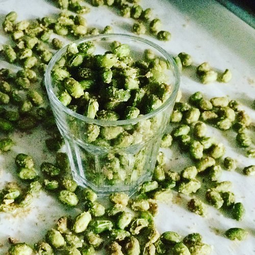 A bowl of crispy roasted edamame seasoned with garlic, shown on a rustic wooden surface, ideal for a plant-based, high-protein snack or trail mix ingredient.